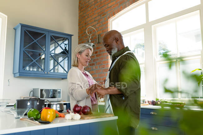 Счастливая пожилая пара, готовящая вместе на кухне, в фартуке. здоровый, активный образ жизни на дому. — стоковое фото