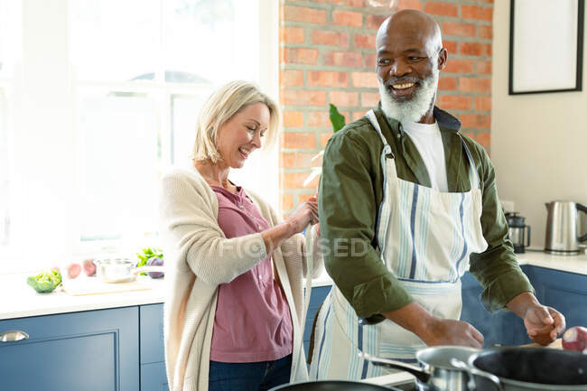 Heureux couple diversifié senior dans la cuisine cuisine ensemble, portant tablier. mode de vie sain et actif à la retraite à la maison. — Photo de stock