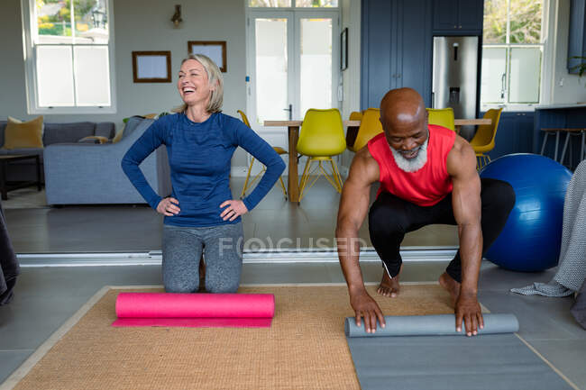 Happy senior diverse couple in exercise clothes practicing yoga together, smiling. healthy, active retirement lifestyle at home. — Stock Photo