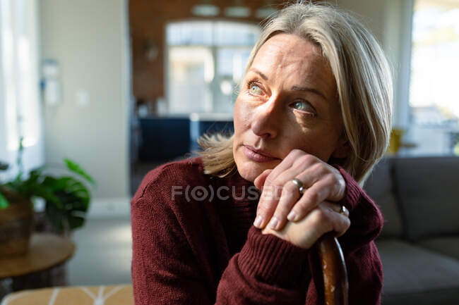 Nachdenkliche ältere kaukasische Frau im Wohnzimmer, die auf dem Sofa sitzt, den Stock in der Hand hält und nachdenkt. Lebensstil im Ruhestand, Zeit zu Hause verbringen. — Stockfoto