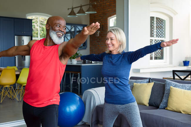 Casal diverso sênior feliz em roupas de exercício praticando ioga juntos, alongamento. estilo de vida saudável e ativo em casa. — Fotografia de Stock