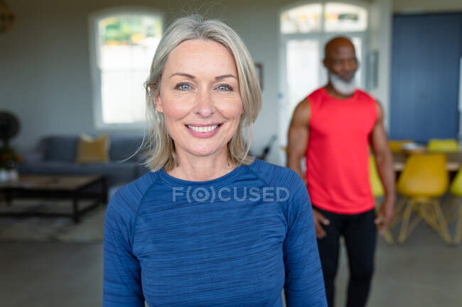 Retrato de feliz pareja mayor diversa en ropa de ejercicio practicando yoga, mirando a la cámara. estilo de vida saludable y activo de jubilación en el hogar. - foto de stock