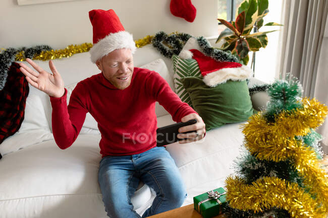 Albino afro-americano vestindo chapéu de Papai Noel fazendo videochamada com decorações de Natal. Natal, festividade e tecnologia da comunicação festividade e tecnologia da comunicação. — Fotografia de Stock