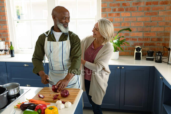 Happy senior diverse couple in kitchen cooking together, wearing apron. healthy, active retirement lifestyle at home. — Stock Photo