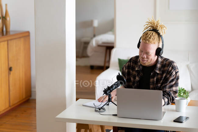 Homem americano africano albino feliz com dreadlocks trabalhando em casa e fazendo podcast. trabalho remoto usando a tecnologia em casa. — Fotografia de Stock