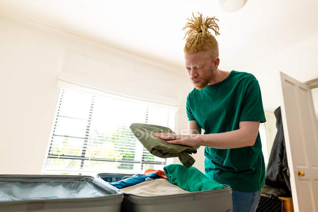 Albino uomo afroamericano che prepara valigia in camera da letto. vacanza e preparazione al viaggio durante la covd 19 pandemia. — Foto stock