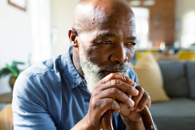 Ragionevole uomo anziano afroamericano in soggiorno seduto sul divano, con in mano un bastone da passeggio. stile di vita di pensione, trascorrere del tempo a casa. — Foto stock