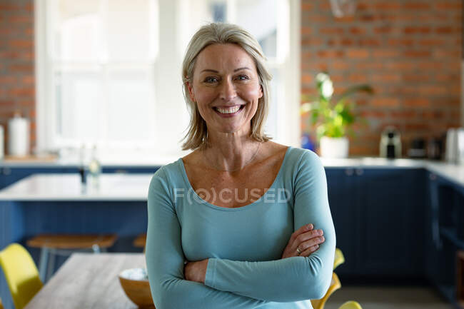 Retrato de mujer caucásica mayor feliz en la cocina, mirando a la cámara y sonriendo. estilo de vida de jubilación, pasar tiempo en casa. - foto de stock