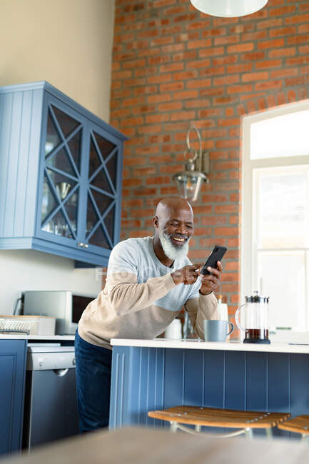 Счастливый старший африканский американец на кухне, использующий смартфон. уход на пенсию образ жизни, дома с технологиями. — стоковое фото