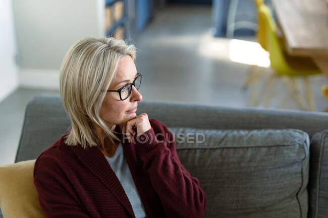 Удумлива старша біла жінка у вітальні сидить на дивані, думаючи. пенсійний спосіб життя, проводити час вдома . — стокове фото