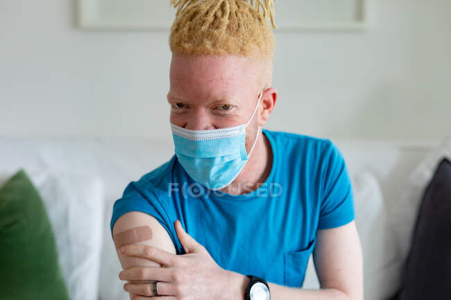 African american albino man wearing a face mask with plaster after vaccination. global covid 19 pandemic and healthcare. — Stock Photo