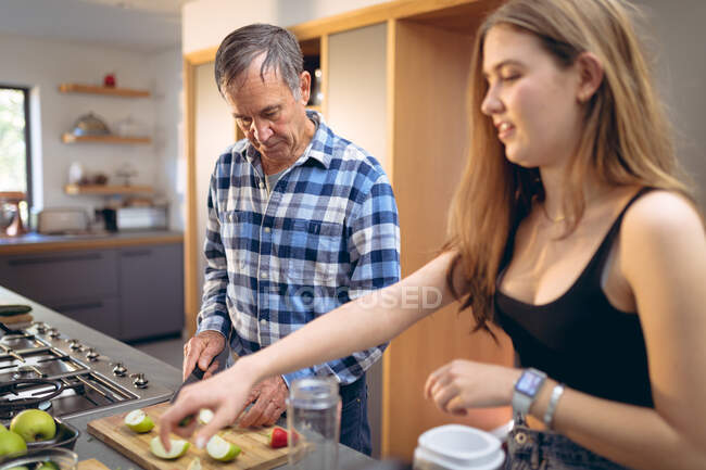 Caucasian grandfather and granddaughter preparing smoothie in kitchen. active and healthy retirement lifestyle at home. — Stock Photo