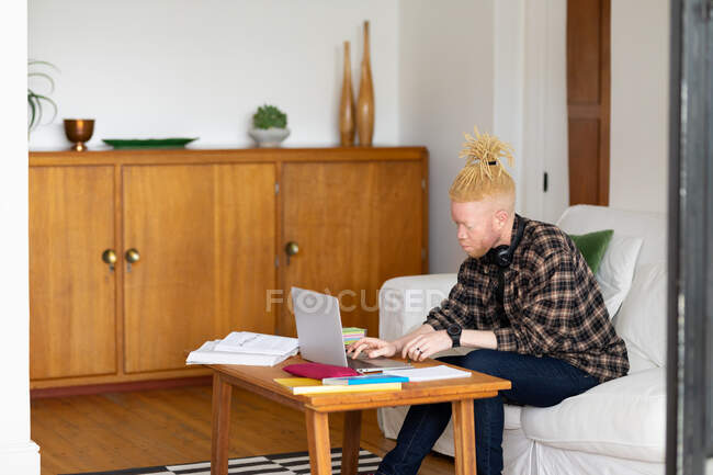 Albino-amerikanischer Mann mit Dreadlocks, der von zu Hause aus arbeitet und Laptop benutzt. Fernbedienung mit Technologie zu Hause. — Stockfoto