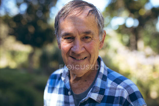 Porträt eines glücklichen kaukasischen Seniors, der im Garten in die Kamera blickt. Aktiver und gesunder Lebensstil im Ruhestand zu Hause und im Garten. — Stockfoto