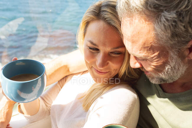 Happy caucasian mature couple drinking coffee and looking through the window. enjoying leisure time at home. — Stock Photo