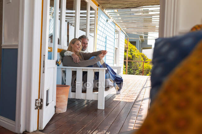 Feliz casal caucasiano sentado no terraço ensolarado. desfrutar de tempo de lazer na casa da frente da praia. — Fotografia de Stock