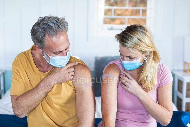 Couple caucasien portant un masque facial montrant du plâtre sur le bras où ils ont été vaccinés. santé et mode de vie pendant la pandémie de covidé 19 — Photo de stock