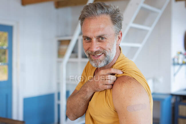 Hombre caucásico sonriente mostrando yeso en el brazo donde fueron vacunados contra el coronavirus. salud y estilo de vida durante la pandemia de covid 19. - foto de stock