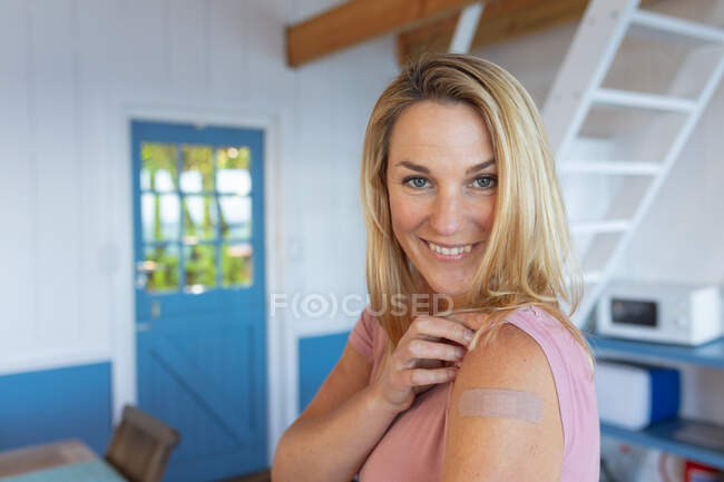 Mujer caucásica sonriente mostrando yeso en el brazo donde fueron vacunados contra el coronavirus. salud y estilo de vida durante la pandemia de covid 19. - foto de stock