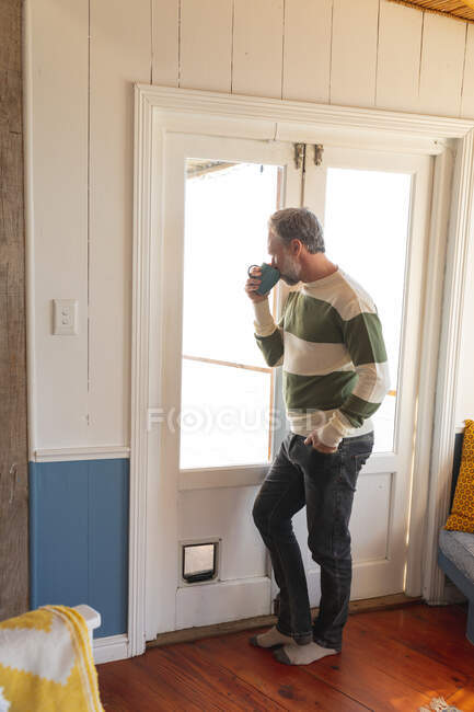 Relaxing caucasian mature man drinking coffee and looking trough the window. enjoying leisure time at home. — Stock Photo