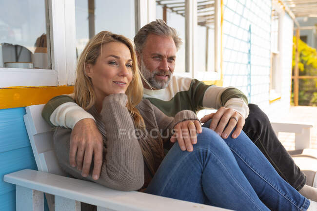 Relajante pareja caucásica sentada en la soleada terraza. disfrutar del tiempo libre en la casa frente a la playa. - foto de stock