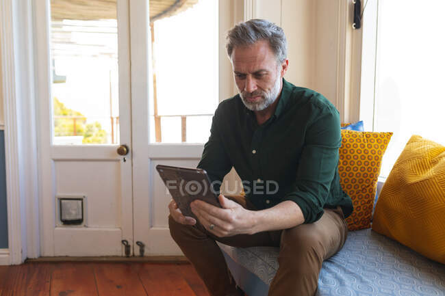 Rilassante uomo maturo caucasico utilizzando tablet in soggiorno soleggiato. godendo del tempo libero a casa. — Foto stock