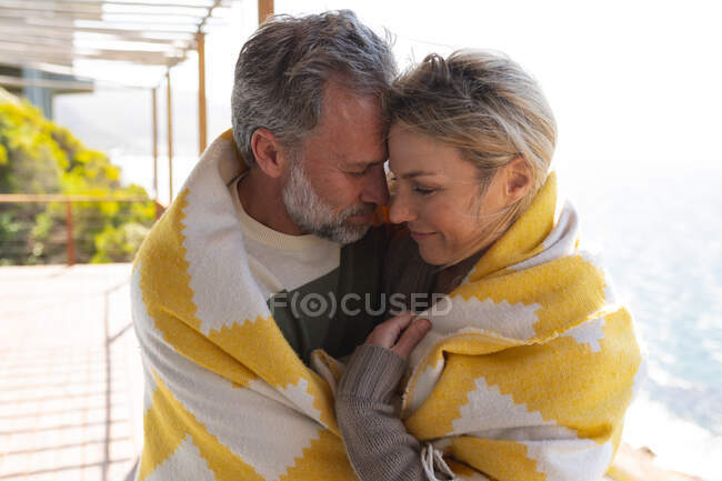 Casal caucasiano relaxante abraçando no terraço ensolarado. desfrutar de tempo de lazer na casa da frente da praia. — Fotografia de Stock