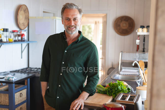 Portrait of happy caucasian mature man in sunny modern kitchen. enjoying leisure time at home. — Stock Photo