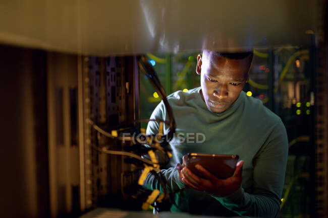 Африканський американський фахівець з комп'ютерних технологій використовує планшет і працює в серверній кімнаті. Digital information storage and communication network technique. — стокове фото