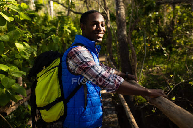 Улыбающийся африканский американец с рюкзаком для прогулок по сельской местности. здоровый, активный уличный образ жизни и досуг. — стоковое фото