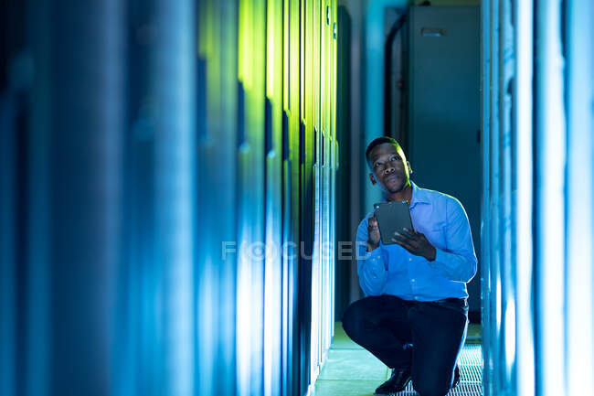 Técnico de computadora afroamericano masculino usando tableta trabajando en la sala de servidores. tecnología de redes digitales de almacenamiento y comunicación de información. - foto de stock