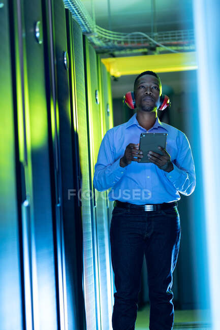 Afrikanisch-amerikanischer Computertechniker mit Kopfhörern und Tablet im Serverraum. digitale Informationsspeicherung und Kommunikations-Netzwerktechnologie. — Stockfoto