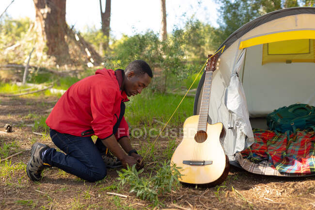 African american man putting up the tent in countryside. healthy, active outdoor lifestyle and leisure time. — Stock Photo