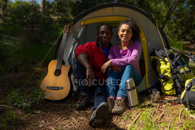 Happy diverse couple sitting in the tent in countryside. healthy, active outdoor lifestyle and leisure time. — Stock Photo