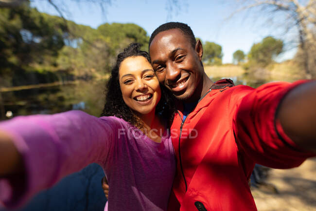 Casal diverso feliz levando selfie no lago no campo. saudável, estilo de vida ao ar livre ativo e tempo de lazer. — Fotografia de Stock