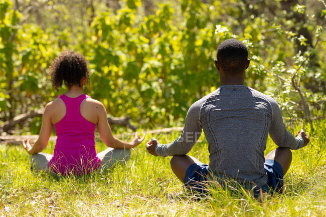 Entspannendes vielfältiges Paar sitzt mit gekreuzten Beinen und meditiert in der Landschaft. gesunder, aktiver Lebensstil und Freizeit im Freien. — Stockfoto