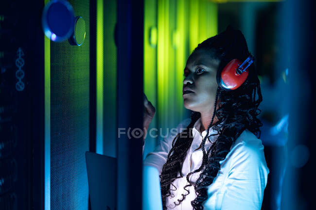 African american female computer technician wearing headphones using tablet working in server room. digital information storage and communication network technology. — Stock Photo