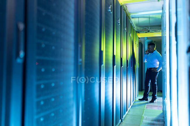 African american male computer technician making call and working in server room. digital information storage and communication network technology. — Stock Photo