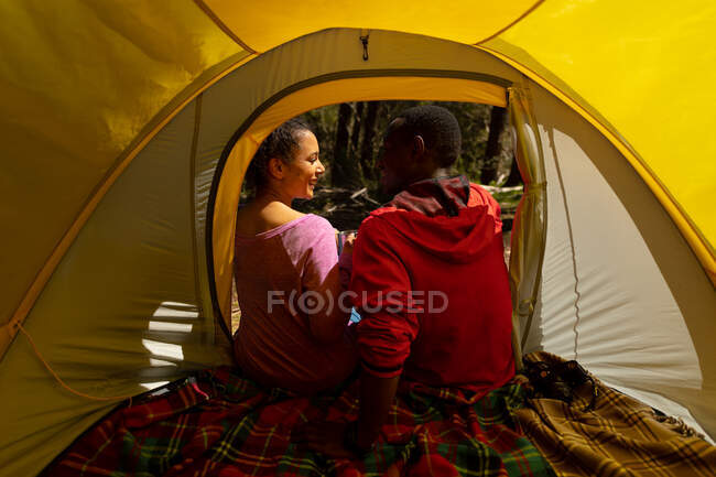 Happy diverse couple sitting in the tent in countryside. healthy, active outdoor lifestyle and leisure time. — Stock Photo