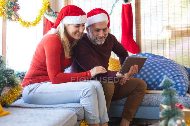 Feliz casal maduro caucasiano fazendo uma chamada de vídeo no Natal, usando tablet. Natal, festividade e tecnologia de comunicação. — Fotografia de Stock