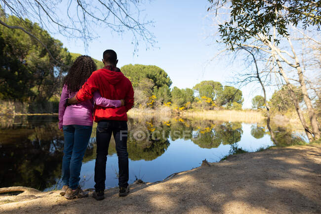 Feliz pareja diversa de pie en el lago en el campo. estilo de vida al aire libre saludable y activo y tiempo libre. - foto de stock