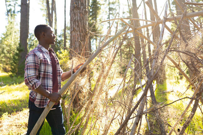 African american man building hut in the forest. healthy, active outdoor lifestyle and leisure time. — Stock Photo