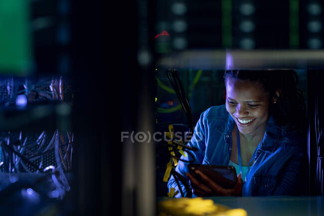 Técnica de informática afro-americana usando tablet e trabalhando na sala de servidores. armazenamento digital de informações e tecnologia de rede de comunicação. — Fotografia de Stock