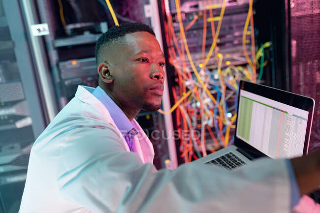 Homme technicien informatique afro-américain utilisant un ordinateur portable travaillant dans la salle des serveurs d'affaires. stockage de l'information numérique et technologie des réseaux de communication. — Photo de stock