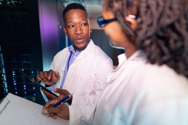 Techniciens informatiques afro-américains utilisant une tablette travaillant dans la salle des serveurs. stockage de l'information numérique et technologie des réseaux de communication. — Photo de stock