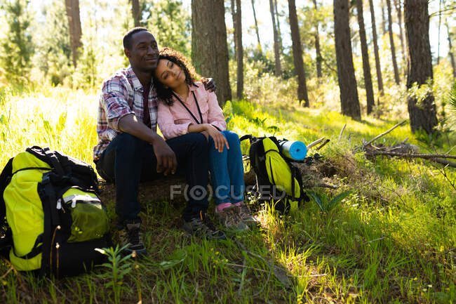 Feliz casal diversificado com mochilas fazendo uma pausa de caminhadas no campo. saudável, estilo de vida ao ar livre ativo e tempo de lazer. — Fotografia de Stock