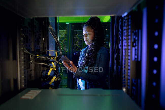Técnico de computadora afroamericana usando tableta y trabajando en la sala de servidores. tecnología de redes digitales de almacenamiento y comunicación de información. - foto de stock