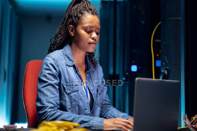 Técnica de informática afro-americana usando laptop trabalhando na sala de servidores. armazenamento digital de informações e tecnologia de rede de comunicação. — Fotografia de Stock