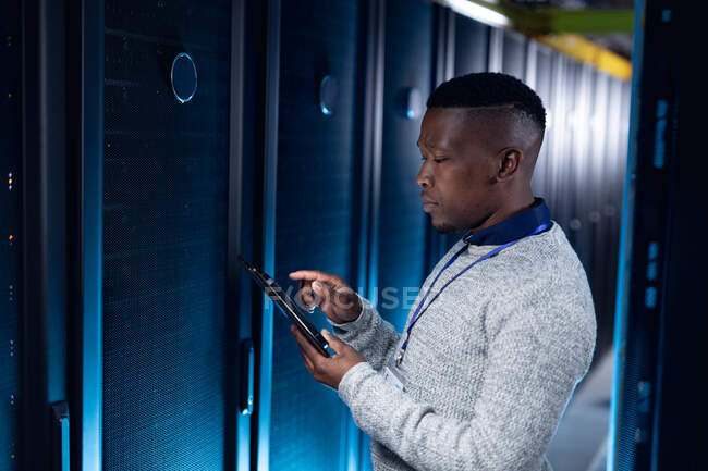 Африканский американец, компьютерный техник, носит наушники, используя планшет, работающий в серверной. цифровые технологии хранения и передачи информации. — стоковое фото