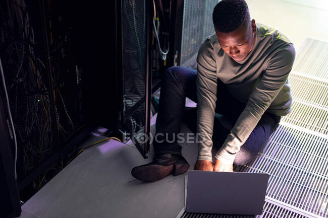 African american male computer technician using laptop working in server room. digital information storage and communication network technology. — Stock Photo
